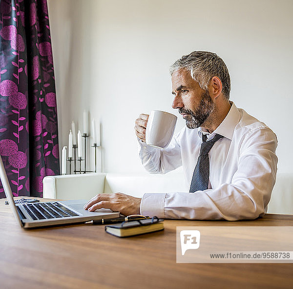 Porträt eines Geschäftsmannes der zu Hause arbeitet und Kaffee trinkt.