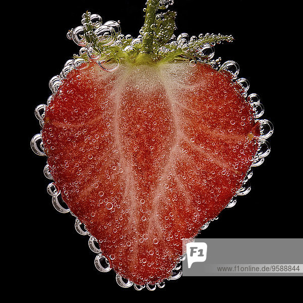 Geschnittene Erdbeere mit Luftblasen vor schwarzem Hintergrund  Nahaufnahme