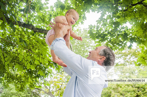 Grandfather lifting up baby granddaughter in park