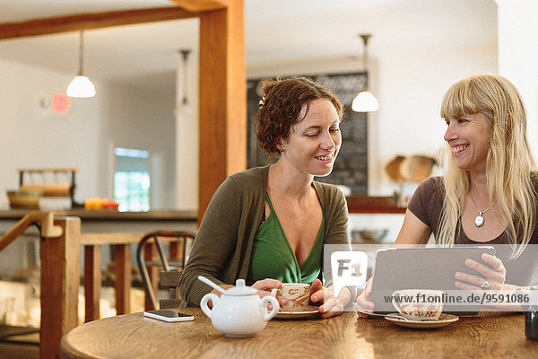 Zwei mittlere erwachsene Freundinnen beim Betrachten des digitalen Tabletts im Country Store Cafe