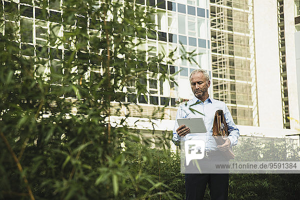 Businessman holding digital tablet outside office building