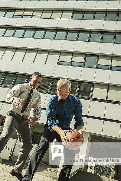 Two businessmen playing basketball outside office building