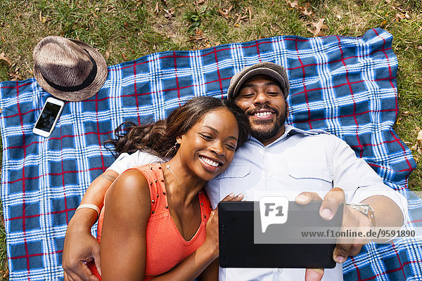 Paar liegt auf Gras und schaut sich den Film auf dem Tablett an.