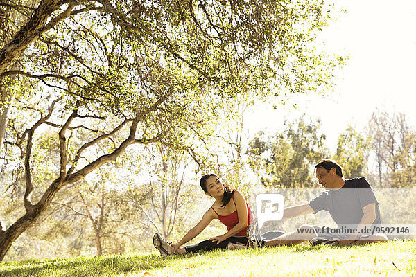 Mature running couple warming up touching toes in park