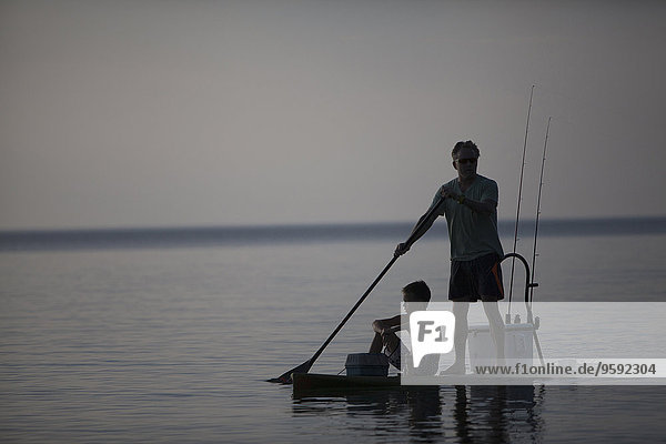 Silhouetted man and teenage son fishing from paddleboard in Lake Superior  Au Train Bay  Michigan  USA