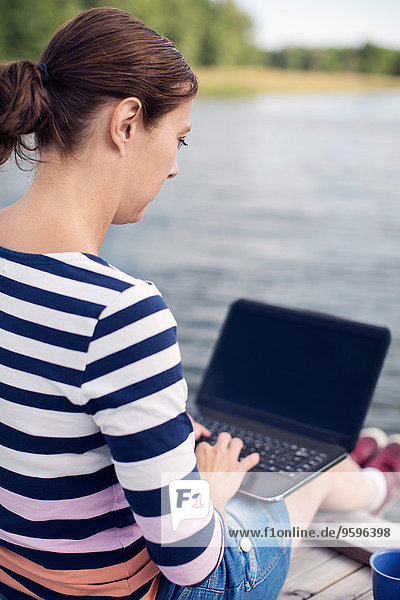 Durchgehende Seitenansicht der reifen Frau mit Laptop am Pier