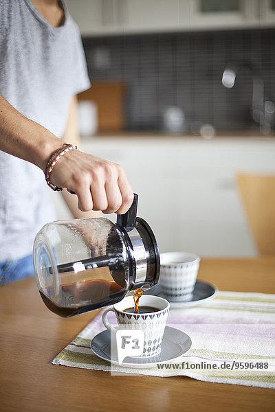 Mittelteil des Mannes der Kaffee in die Tasse am Tisch gießt.