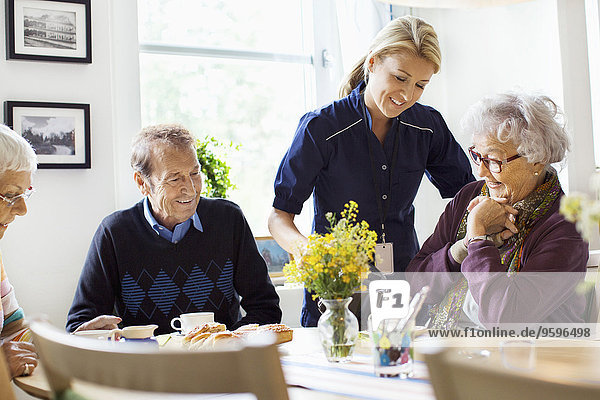 Lächelnde Frau serviert Kaffee für Senioren im Pflegeheim