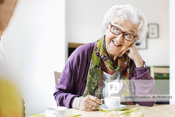 Glückliche Seniorenfrau beim Kaffeetrinken am Frühstückstisch im Pflegeheim