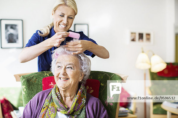 Glückliche Frau  die Lockenwickler an den Haaren der älteren Frau im Pflegeheim anbringt.