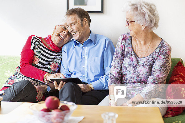 Glückliches Seniorenpaar mit digitalem Tablett von einer Freundin im Pflegeheim