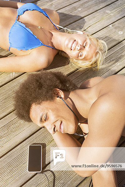 Ein Paar  das Musik hört  während es sich auf der Strandpromenade ausruht