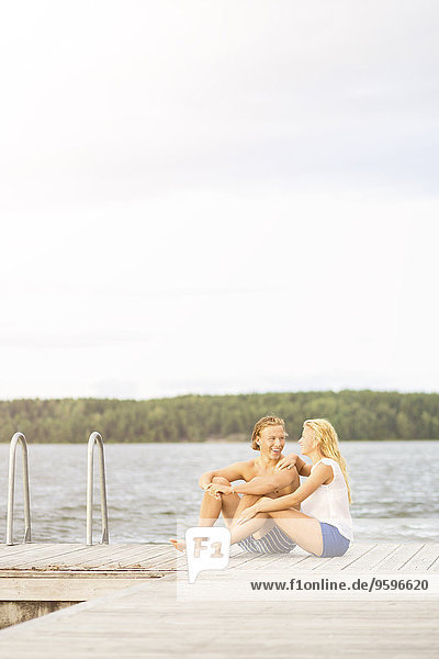 Paar sitzt auf einer Strandpromenade am See gegen den Himmel