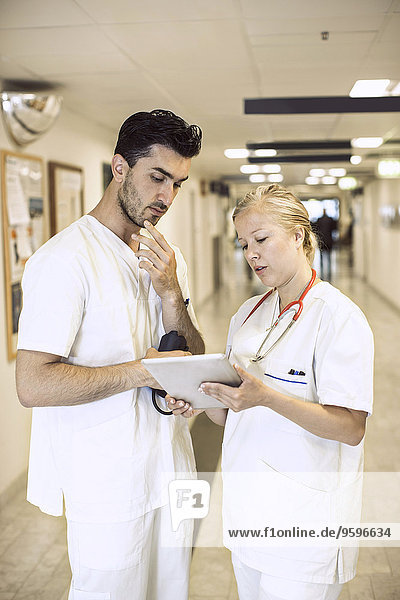 Doctors discussing over digital tablet in hospital corridor