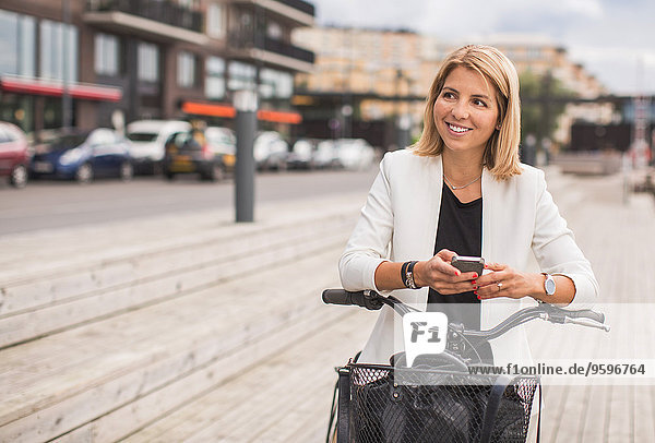 Lächelnde Geschäftsfrau mit Smartphone in der Stadt