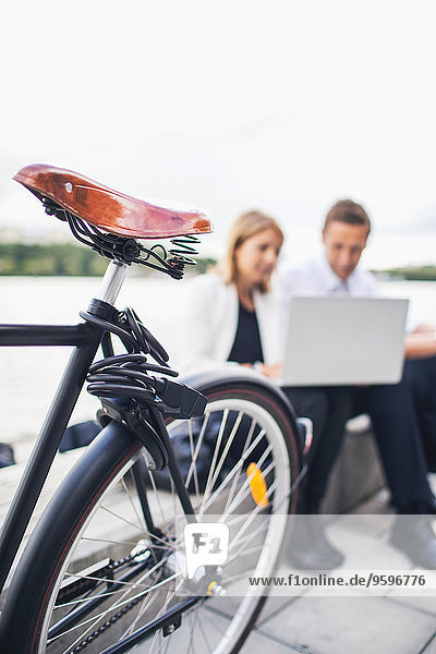Abgeschnittenes Bild des Fahrrads auf dem Bürgersteig mit Geschäftsleuten  die am Laptop gegen den klaren Himmel arbeiten.