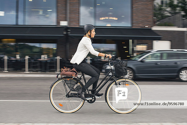 Volle Länge der Geschäftsfrau beim Fahrradfahren auf der Stadtstraße
