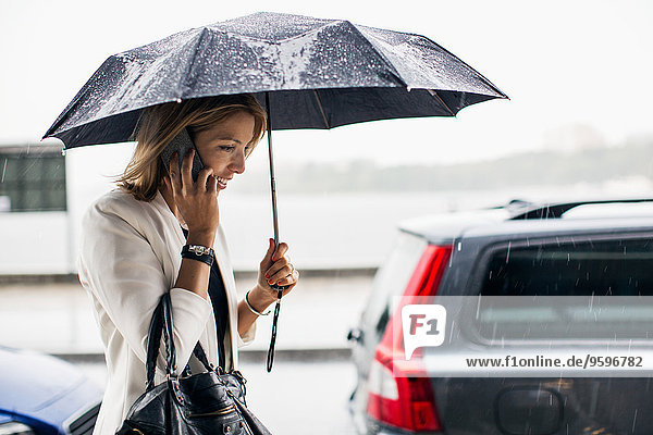 Geschäftsfrau im Gespräch mit Smartphone während der Regenzeit in der Stadt