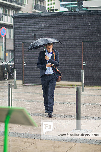 Volle Länge des Geschäftsmannes,  der während der Regenzeit auf dem Bürgersteig läuft.
