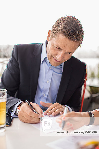 Geschäftsmann unterschreibt Papierkram im Außencafé gegen klaren Himmel