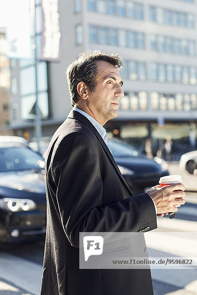 Seitenansicht des Geschäftsmannes  der weg schaut  während er eine Einweg-Kaffeetasse in der Stadt hält.