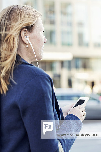 Geschäftsfrau beim Musikhören über Kopfhörer mit dem Handy auf der Straße