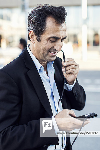 Businessman communicating through headphones while using mobile phone on street