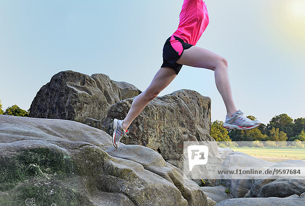 Neck down Ansicht einer jungen Läuferin  die über eine Felsformation springt.