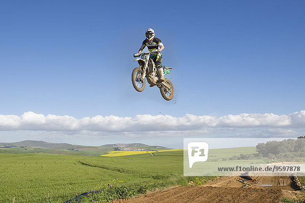 Junge männliche Motocrosser springen in der Luft über die Landschaft
