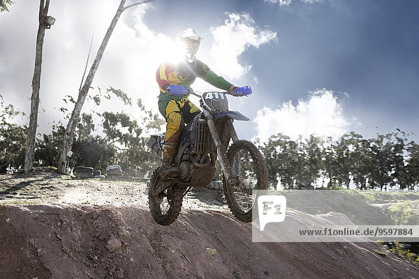 Junger männlicher Motocross-Rennfahrer springt in der Luft den Schlammberg hinunter