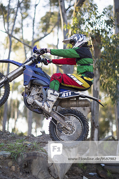 Junger männlicher Motocross-Rennfahrer  der über Baumstämme auf Waldwegen fährt