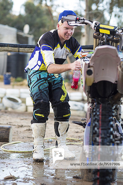Young male motocross competitor cleaning motorcycle