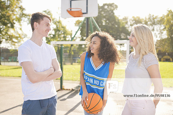 Three young adult basketball players chatting on basketball court