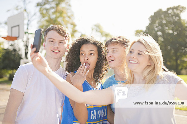 Vier junge erwachsene Basketballspieler mit Smartphone Selfie auf dem Platz