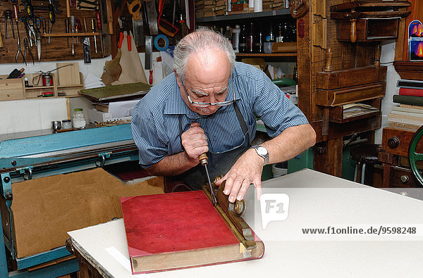 Senior Mann beim Restaurieren von Büchern in der traditionellen Buchbinderei