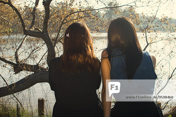 Zwei junge Frauen sitzen am See  Rückansicht