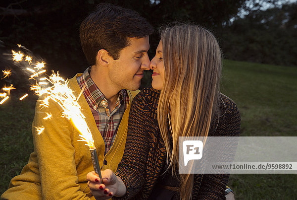 Young couple nose to nose in park holding sparkling firework