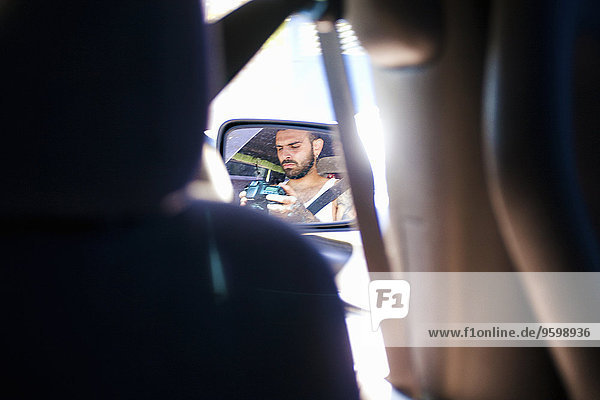 Reflektion des jungen Mannes im Auto-Außenspiegel