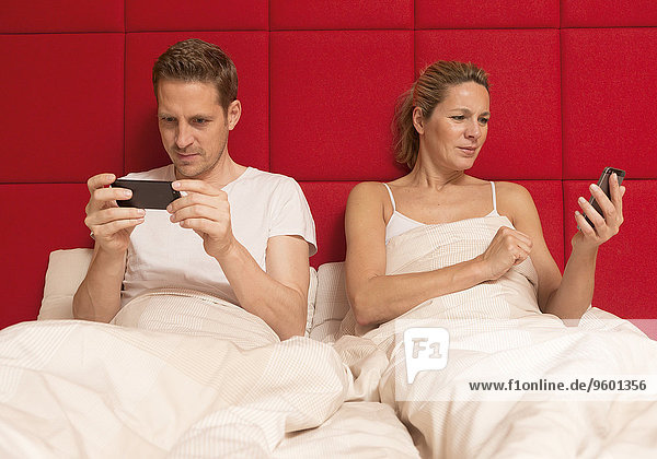 Paar liegt im Bett  jeder schaut auf sein Smartphone