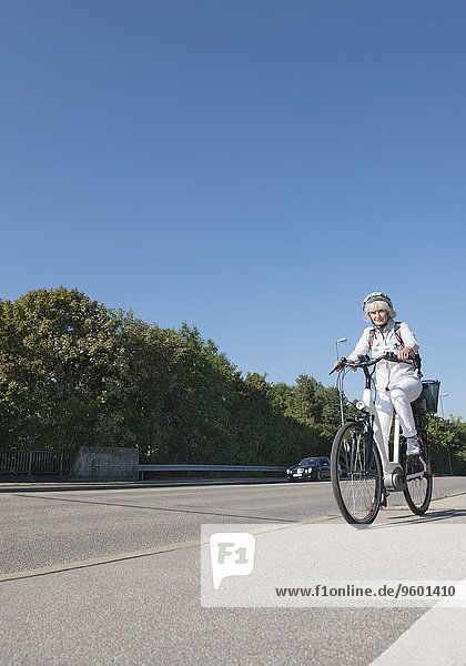 Seniorin fährt mit E-Bike auf Fahrradweg