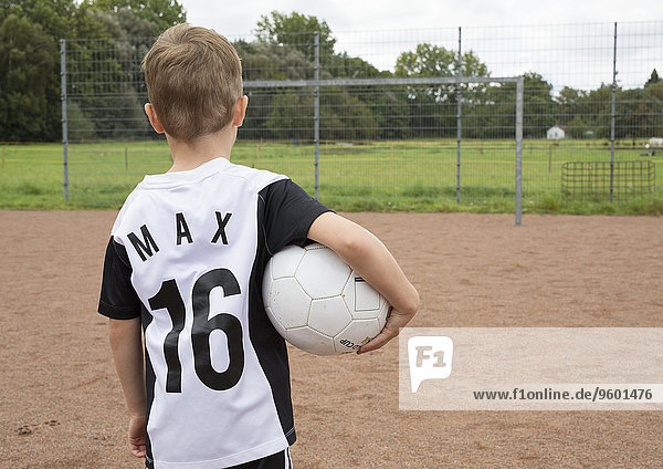 Kleiner Junge auf Sportplatz  von hinten mit Ball unter dem Arm