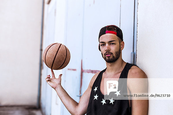Portrait of young man balancing basketball wearing basecap