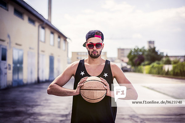 Porträt eines jungen Mannes mit Basketball mit Basecap und Sonnenbrille