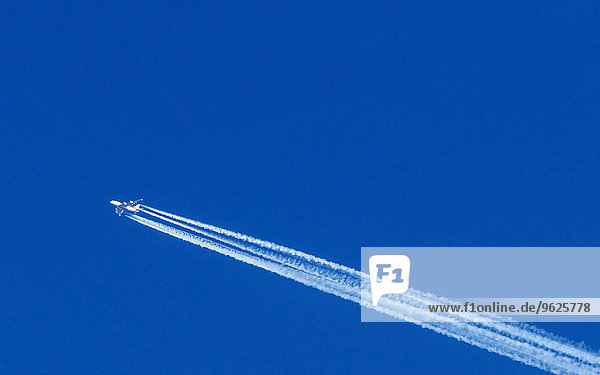 Flying airplane and vapour trail in front of blue sky