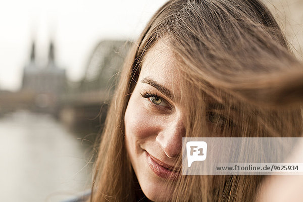 Deutschland  Köln  Porträt einer lächelnden jungen Frau  die mit ihren Haaren spielt.