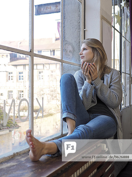Junge Frau mit Teeschale auf Fensterbank sitzend
