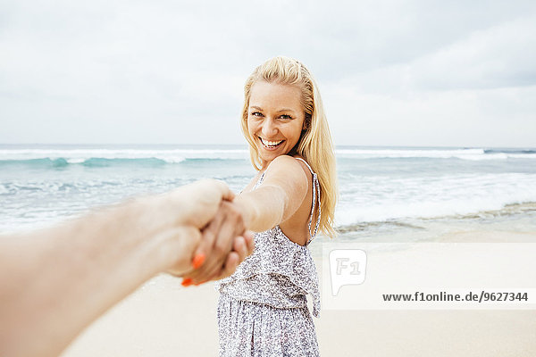 Indonesien  Bali  lächelnde Frau am Strand zieht Hand eines Mannes