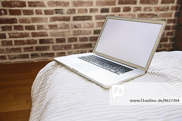 Laptop auf dem Bett stehend vor der Ziegelwand