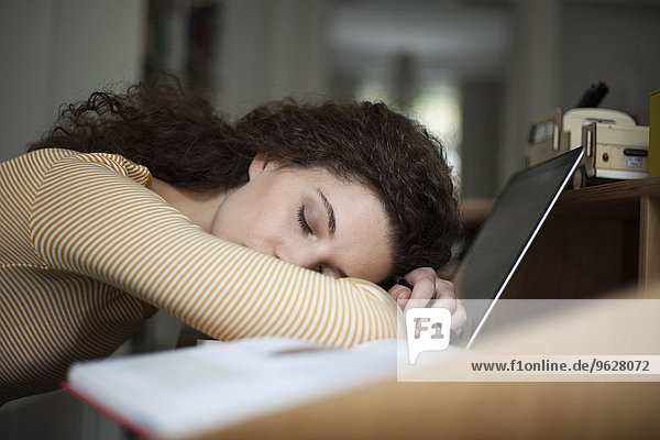 Überarbeitete junge Frau schläft auf dem Laptop im Home-Office
