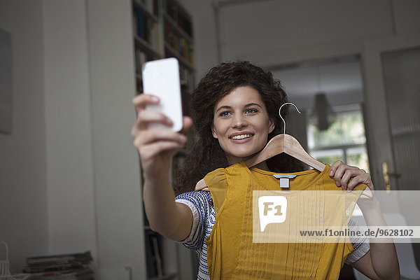 Junge Frau zu Hause mit einem Selfie mit Kleidungsstück